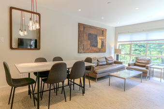 The dining and living area features a modern dining table, comfortable seating, and a large window offering an exterior view.