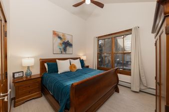 The bedroom at Aspen Trail Junction features a wooden sleigh bed with a blue comforter and pillows, flanked by two wooden nightstands with lamps.