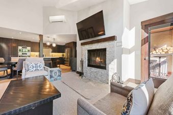 An open-concept living room and kitchen at The Charter B440, featuring a fireplace with a large TV above, comfortable seating, and a modern kitchen.