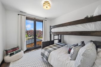 A cozy bunk room at Grandview Escape with a dark wood bunk bed, checkered and striped bedding, a textured rug, and a balcony with an exterior view.