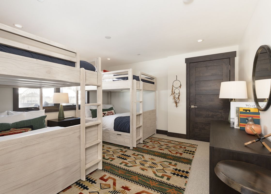The bunk room at Spanish Peaks Highlands Cabin 36 features two light wood bunk beds, a colorful area rug, and a dark wood console with a mirror.