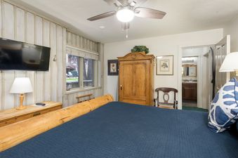 The primary bedroom features a comfortable bed with a dark blue comforter, wooden furniture, and a ceiling fan.