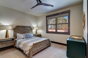 A bedroom with a wooden bed and a large window with a view of the forest outside.
