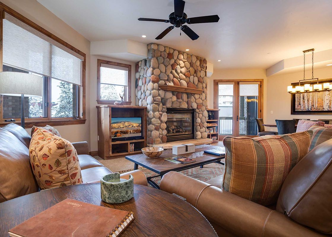 A cozy living room at Chateau Chamonix CX313 features a stone fireplace, leather sofas, a coffee table, and an adjacent dining area.