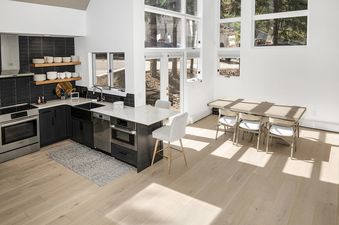 The open-concept kitchen and dining area of Rockledge 325 features modern appliances, dark cabinetry, marble countertops, and a dining table with chairs, all illuminated by abundant natural light from large windows.