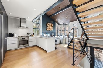 A modern kitchen with white cabinets and stainless steel appliances flows into an open-concept living room with a fireplace and large windows at the Rockledge Chalet.