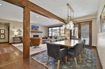 The image showcases the elegant, open-concept living and dining area of Silver Star 2101, featuring a large dining table, a cozy living room with a stone fireplace, and expansive windows.