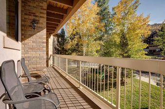 A private balcony at Chateau Chamonix CX332 with outdoor seating, brick walls, and a stunning view of golden aspen trees and mountains in the autumn.