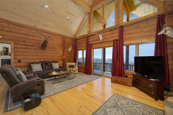 The living room at 2665 Golden Eagle Drive features a warm and inviting atmosphere with wooden walls, comfortable seating, and large windows offering picturesque views of the snowy landscape.
