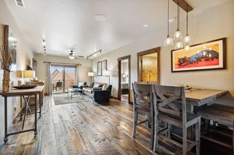 A wide-angle view of an open-concept living room and dining area, featuring rustic wood floors, a cozy lounge with a sofa, a dining table with bar stools, and a balcony with outdoor seating.