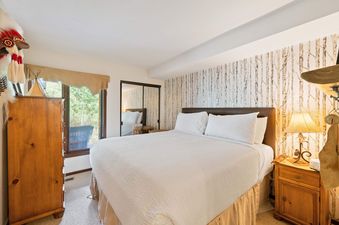 A serene bedroom at Ridgepoint Townhome 192 featuring a comfortable bed with white linens, a birch tree accent wall, and a view of lush greenery outside the window.