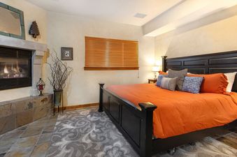 A cozy bedroom in Bear Hollow 5428, featuring a dark wood bed with orange bedding, a tiled fireplace, and a large window with wooden blinds.