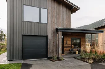 The Lodge Cabins features a modern rustic exterior with dark corrugated metal and warm wood siding, a large black garage door, and a welcoming covered entrance with outdoor seating.