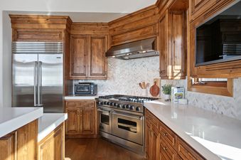A modern kitchen at Bellemont 5 with rich wooden cabinets, stainless steel appliances, white countertops, and a chevron backsplash.