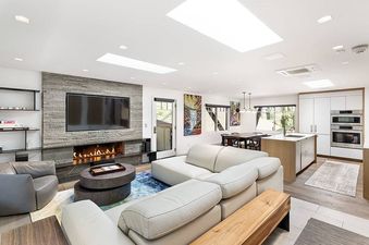 A modern open-concept living space with a large TV mounted above a fireplace, a sectional sofa, a dining area, and a contemporary kitchen.