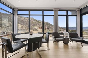 A modern dining table and lounge seating in One Snowmass West 301, surrounded by floor-to-ceiling windows showcasing mountain views.
