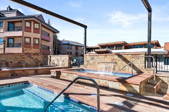 A resort style outdoor pool with a hot tub and a stone wall with small waterfalls.