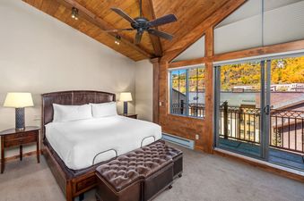 The bedroom at Landmark 702 features a king bed with a leather headboard, a vaulted wooden ceiling, and a private balcony with mountain views.