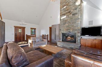 The grand living area at Ridge Top Chalet featuring a stone fireplace, leather sofas, and a large wooden coffee table under vaulted ceilings.