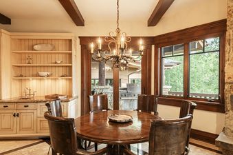 An elegant dining area at Park City Colony at Elite Elevation with a round wooden table, a rustic chandelier, and a built-in wet bar.