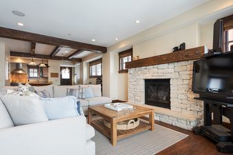 A spacious living area at Silver Star 404, featuring a light-colored sectional sofa, a rustic wooden coffee table, a stone fireplace, and a television, with a view of the kitchen and dining area in the background.