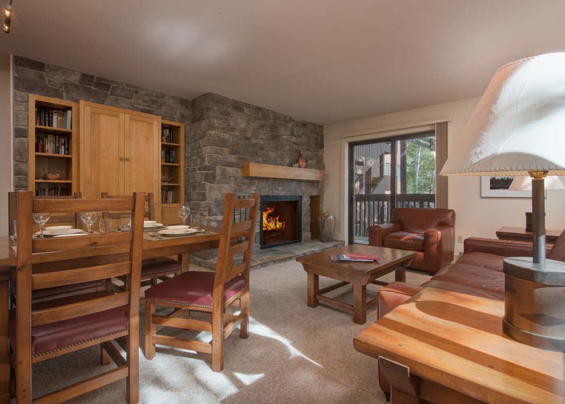 A cozy living room with a fireplace, a large leather couch, and a wooden dining table set.