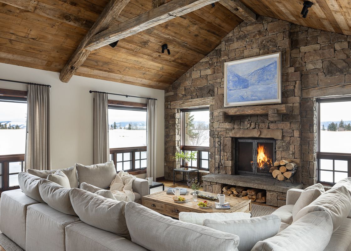 Cozy living room with a stone fireplace, large sofas, and snowy views through the windows at Shooting Star Cabin 04.