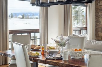 Warm, elegant dining area in Shooting Star Cabin 04 with a live-edge table, leather chairs, and winter mountain views.