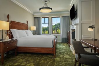 A well-appointed bedroom at the Montage Deer Valley Suite Vista View with Fire Pit, featuring a large bed, elegant decor, and a view of a lush forest through large windows.