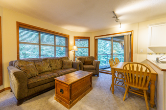 A cozy living area with a plush sofa, a wooden coffee table, and a dining table with chairs, all bathed in warm light.