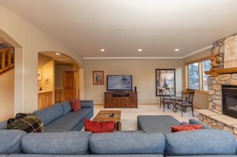 The comfortable and inviting living area features a large blue sectional sofa, a flat-screen TV, a stone fireplace, and a dining nook, offering a perfect setting for relaxation.