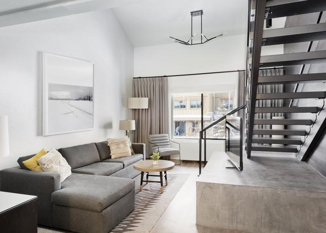 Modern living area of the Gravity Haus JH Loft with a gray sectional sofa and an open-tread staircase.