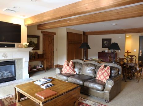 A spacious and inviting living area in The Chateaux Deluxe Studio features a comfortable brown leather sofa, a wooden coffee table, and a grand fireplace.