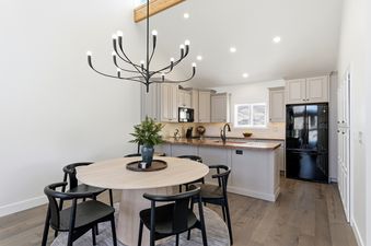 A modern open concept kitchen and dining area with a round dining table and black chairs, a black chandelier, gray kitchen cabinets, and a black refrigerator.