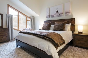 A bedroom with a large bed, a white rug, and a window with a view of the mountains.