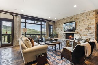 A cozy living room at Arrowleaf Lodge 415 with a stone fireplace, comfortable seating, and large windows offering a scenic mountain view.