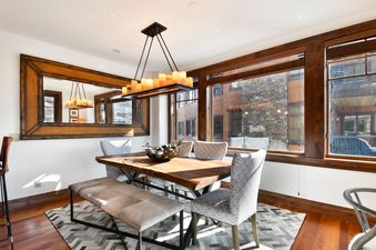 A dining area at Silver Strike Lodge 605 is elegantly appointed with a wooden dining table, a long bench, patterned chairs, and a large mirror reflecting the space.