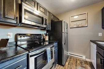 A modern kitchen with stainless steel appliances, black countertops, and dark wood cabinets.