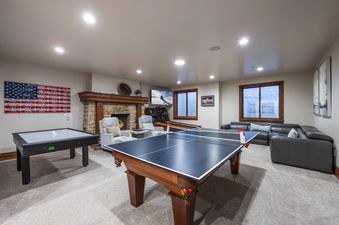 A modern games room with a ping-pong table, air hockey, a fireplace, and a large sofa at Canyons Red Pine Chalet 91.