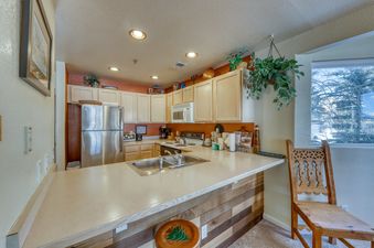 A kitchen with stainless steel appliances, light wood cabinets, and a breakfast bar with a wooden stool.