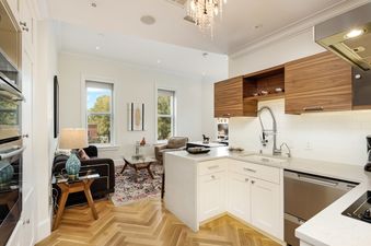 A modern kitchen with stainless steel appliances, white cabinets, and a wood countertop. There is a large window in the background looking out onto a city street.