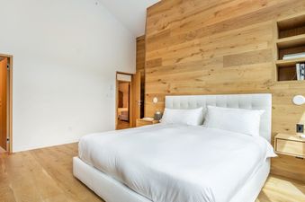 Modern bedroom in Tyrolean 6 with a wooden accent wall, white bed, and vaulted ceiling.