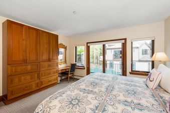 The bedroom in Plaza Lodge 3 Bedroom Gold Unit 4 features a large wooden wardrobe, a vanity with a mirror and chair, a comfortable bed with a patterned duvet, and windows offering a view of the surrounding resort.