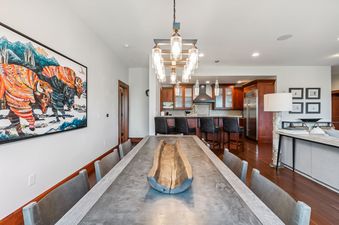 A wide-angle interior shot of the Hummingbird Chateau dining and kitchen area featuring a large dining table with chairs, a decorative wooden centerpiece, and a modern chandelier overhead.