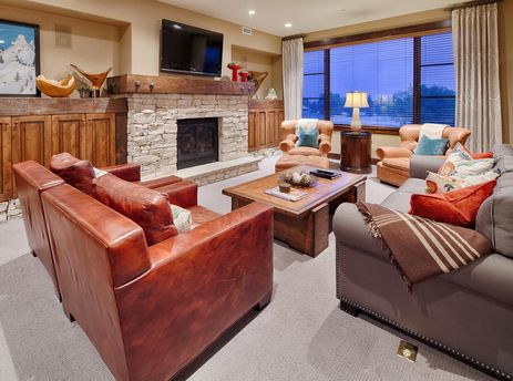 A cozy living room at Silver Star 1201 featuring a gray sofa, brown leather armchairs, a wooden coffee table, and a stone fireplace, with a window offering an outdoor view.