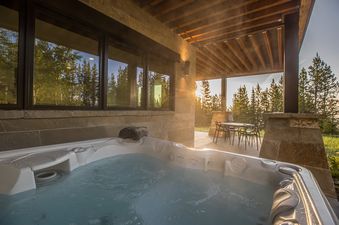 A private outdoor patio with a bubbling hot tub and an outdoor dining set, surrounded by tall trees and lush greenery.