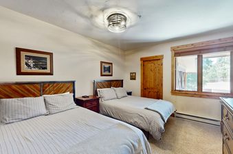 Two beds with striped bedding in a bedroom with a wooden door and a window with a view of trees outside