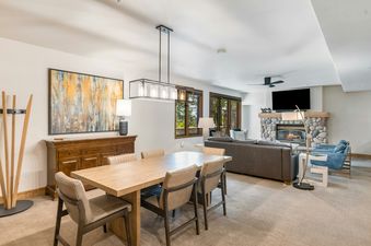 The open-concept living and dining area in Christie Club 306 features a large dining table, a comfortable living room with a stone fireplace, and a large flat-screen TV.