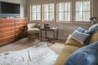 A cozy bedroom at Moonlight Mountain 2 Lower Mountain Road with a wooden dresser, TV, armchair, side table, sofa, and windows with tree views.