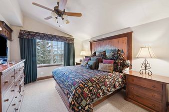 A master bedroom at The Charter G420 featuring a large bed with a patterned quilt, a wooden headboard with a mountain painting, and a large window with green drapes.